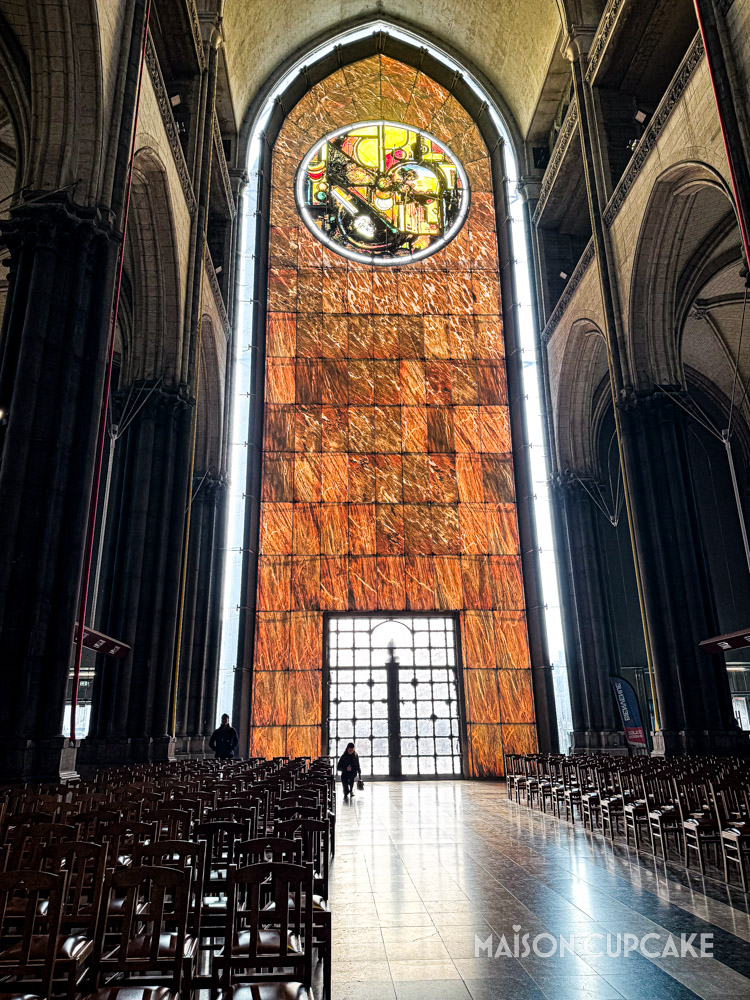Sunlight shining through tall orange coloured modern stained glass window in Lille Cathedral.