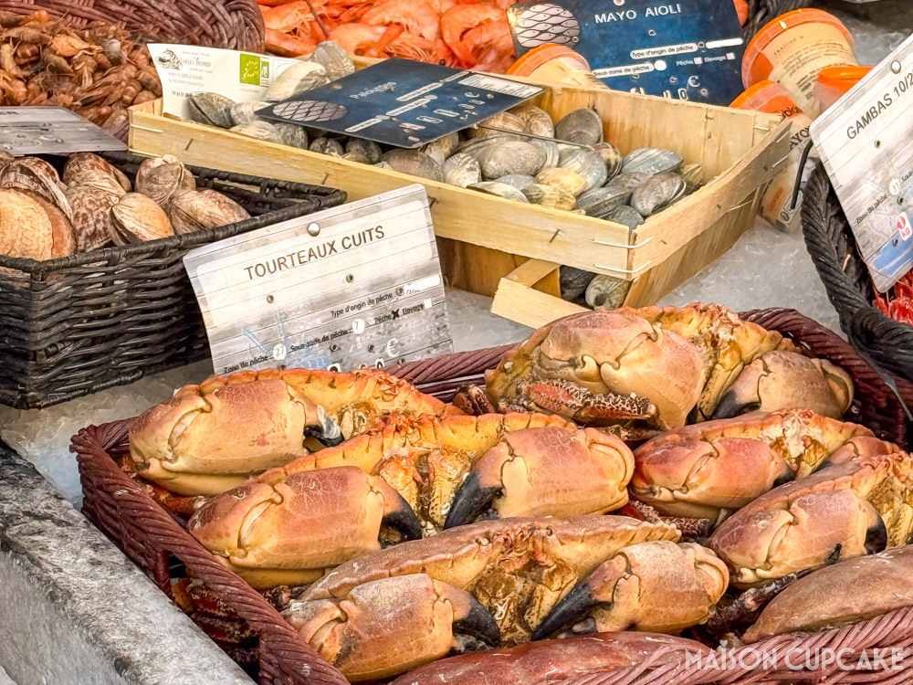 Close up of cooked crabs at Le Crotoy fishmonger stall in northern France. Smaller shellfish in background.