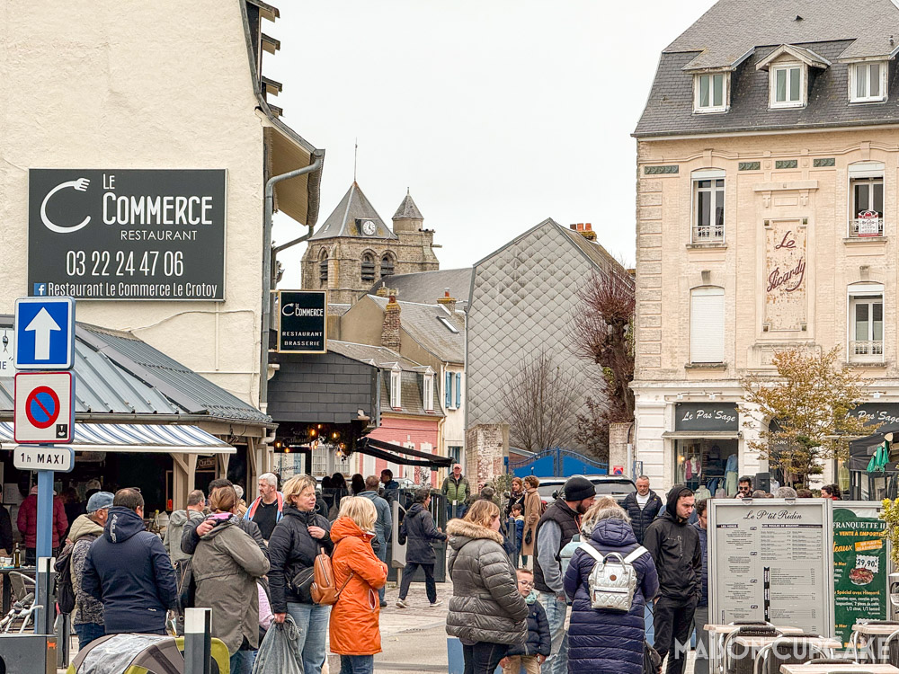 Street scene in Le Crotoy on overcast day; restaurant signage and church tower.