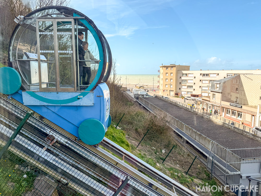 Round blue carriage of Le Tréport cliff railway overlooking the sea and buildings on sunny day.