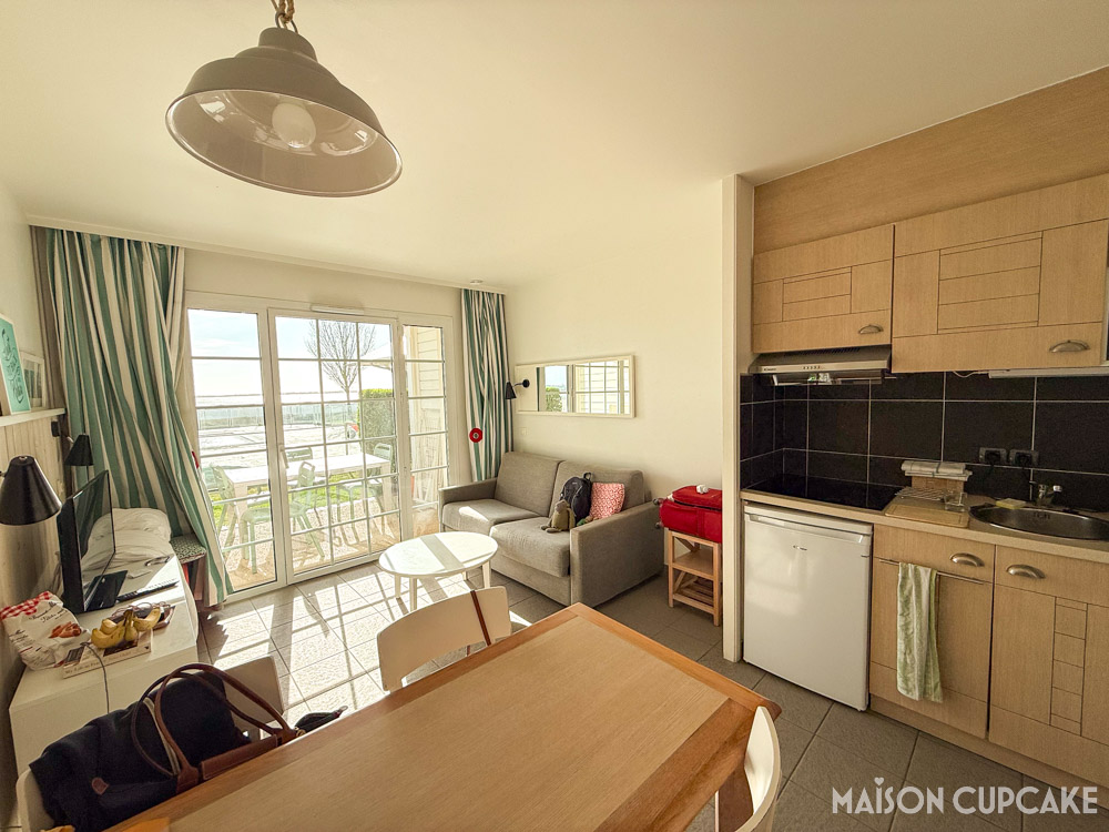 Studio apartment interior at Pierre et Vacances in Le Crotoy; kitchenette, sofa bed and dining table with bright terrace view over the pool and bay.